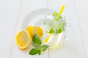 Fancy cool glass of lemonade with ice and mint, Mason jar style cup with yellow straw, green leaves of fresh mint and lemons, one