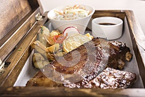 Fancy dish with grilled pork ribs, barbecue sauce, French fries, Coleslaw salad, in a wooden box