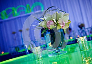 Fancy orchid cocktail flower arrangement and candles on green lucite table set up for a party top view with reflection