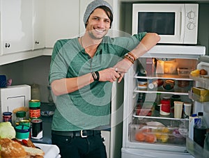 Fancy a snack. Portrait of a smiling young man standing by an open fridge in his kitchen.
