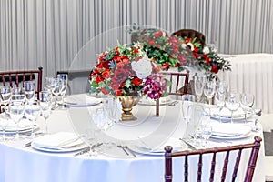 Fancy table set for dinner with flower composition in restaurant, luxury interior background. Wedding elegant banquet decoration