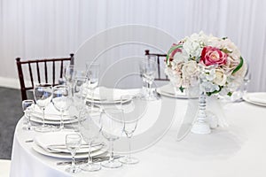 Fancy table set for dinner with flower composition in restaurant, luxury interior background. Wedding elegant banquet decoration