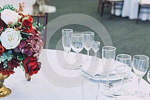 Fancy table set for dinner with flower composition in restaurant, luxury interior background. Wedding elegant banquet