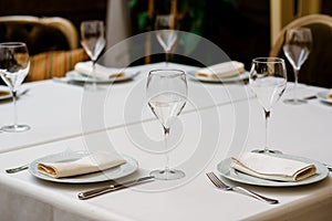 Fancy table set for dinner with flower composition in restaurant, luxury interior background. Wedding elegant banquet