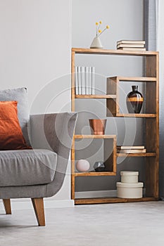 Fancy wooden bookshelf with vases and boxes next to grey scandinavian couch