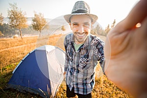 Fanny bearded man smiling and taking selfie in mountains from his smart phone.