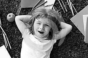 Fanny smiling face of cute smart school boy, lie on grass. Happy pupil.