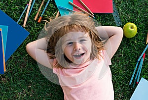 Fanny smiling face of cute smart school boy, lie on grass. Happy pupil.