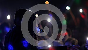 Fans Raise Hands and takes a photos in Front of Bright Colorful Strobing Lights at a concert in a night club.