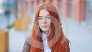 Fantastic attractive young red-haired girl in brown business jacket, on urban street, looking in the camera Steadicam