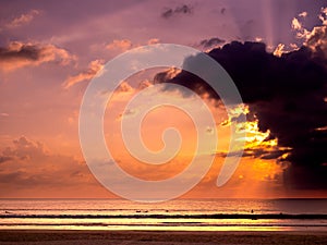 Fantastic background of gradient color sunset sky with beautiful sun rays behind dark cloud over the sea water. Summer sand beach