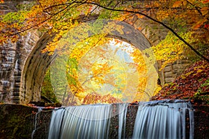 Fantastic Fall Autumn landscape - river waterfall in colorful autumn forest park with yellow red leaves with old bridge