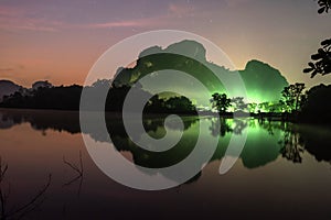 Fantastic landscape lake and mountains in the night with starry backgrounds. Lighting of village in front of the mountain. Sunrise