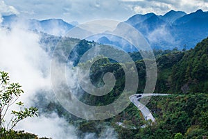 Fantastic mountain road in the mist, aerial view of curve asphalt road and two cars driving to the mountains peak, majestic blue