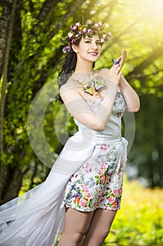 Fantastic Portrait Positive Sensual Brunette Female in White Dress Outdoors. Posing with Flowery Chaplet and Butterfly Against