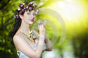 Fantastic Portrait of Sensual Brunette Female in White Dress Outdoors. Posing with Flowery Chaplet and Butterfly Against Sunlight