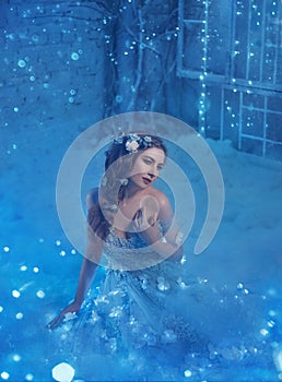 Fantastic snow queen in a luxurious dress, in an ice room. The interior fills with magic, her dress sparkles and glows