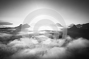 Fantastic sunrise on the top of the rocky mountain with view into misty valley. Black and white