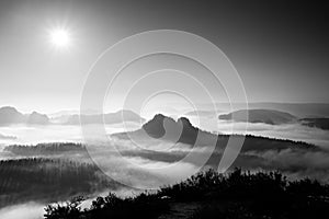 Fantastic sunrise on the top of the rocky mountain with view into misty valley. Black and white