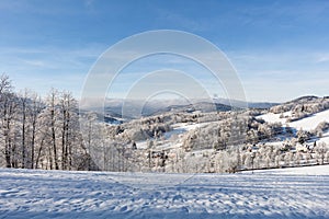 Fantastic winter landscape with wooden house in snowy mountains. Hight mountain peaks in foggy sunset sky. Christmas and winter