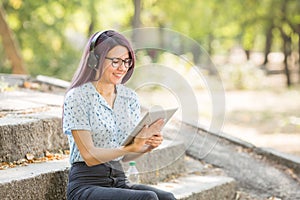 Beautiful young girl studying on a tablet on a park background. Self-education concept. Copy space.