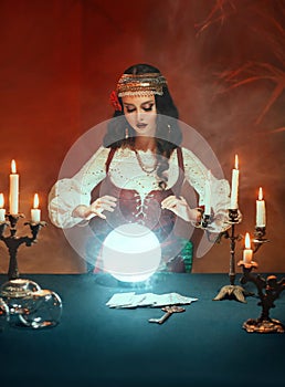 Fantasy beautiful gypsy girl, predicts fate, feel energy of crystal ball in dark gothic room. Mystical photo of old art