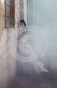 fantasy bride leaning agaisnt rustic wall surrounded by fog