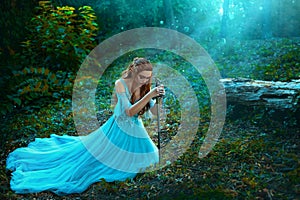 Fantasy elf woman princess warrior sits in forest on green grass holding weapon medieval sword in hands. Warlike queen