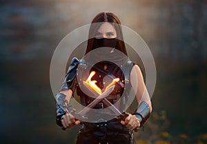 Fantasy fighting woman assassin holds in hands burning daggers. Red-haired girl warrior in black leather costume. ninja