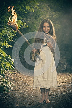 Fantasy girl in rustical white dress deep in forest with lit torch and baby fox
