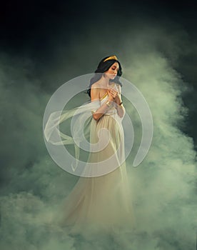 Fantasy Greek goddess woman fashion model walks in dark sky clouds. Girl Aphrodite sexy queen old style myth. White