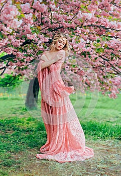 Fantasy happy woman princess walks in spring blooming garden hugs herself by shoulders. Pink flowers sakura tree summer