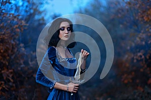 Fantasy medieval woman warrior queen holding dagger, knife in hands. Royal velvet vintage blue dress with pearls, girl