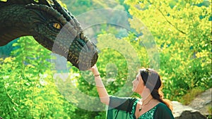 Fantasy portrait woman queen, hand touches muzzle of ancient dragon. Green vintage silk dress golden crown, fabric fly