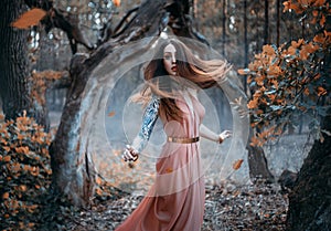 Fantasy portrait of a young red-haired woman in the autumn forest. The nymph girl runs and looks around. Long hair