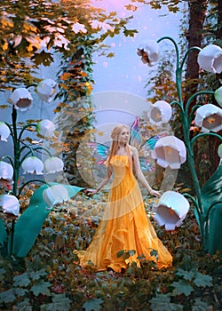 A fantasy woman forest fairy. Fashion model in yellow dress with butterfly wings walks in autumn nature. Large flowers
