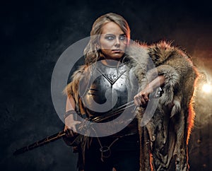 Fantasy woman knight wearing cuirass and fur, holding a sword scabbard ready for a battle. Fantasy fashion. Cosplayer as