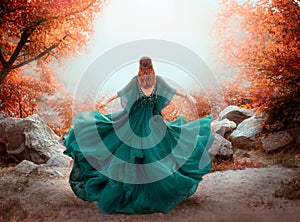 Fantasy woman queen red hair runs in autumn forest. Girl in long elegant royal evening vintage green dress. silk fabric