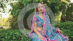 fantasy woman sits on green grass ivy, enjoy summer green nature, tropical garden park. National India blue pink dress