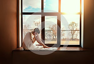 Fantasy young beautiful woman sitting on windowsill panoramic window. Romantic girl waiting for love, sky sunset sun