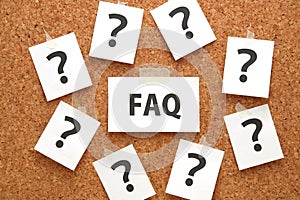 FAQ on a piece of paper and many question marks on a brown cork board.