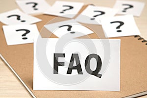 FAQ on a piece of paper and many question marks on notebook.
