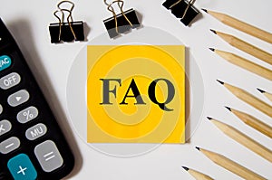 FAQ the word is written on a yellow piece of paper on a white background near a calculator and a pen