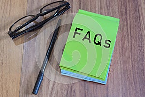 FAQs text on green notepad with glasses and pen on a desk