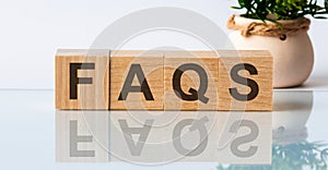 FAQS is a word written in black letters on wooden cubes located on a white mirror surface