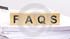 FAQS written on a wooden cube with white paper background, business concept