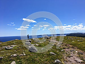 A far away shot of two males at the edge of a rocky headland or cliff overlooking the Atlantic Ocean on a sunny day hiking