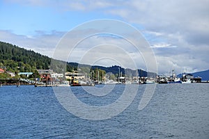 A far away wide view from the ocean looking on land of the port and town of Queen Charlotte, surrounded by forest, in Haida Gwaii