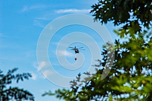 A far distance shot of a helicopter carrying a water tank.