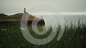 Far view yoga woman exercising on hill top. Girl meditating sitting lotus pose.